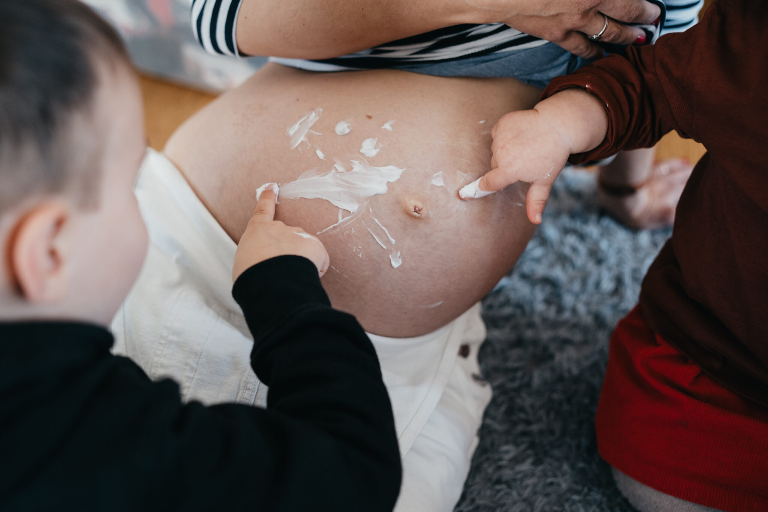 Babybauch Fotografie, Geschwister freuen sich auf das neue Baby, Familienfotografie, Freiburg im Breisgau, große Geschwister malen den Babybauch der Mama an