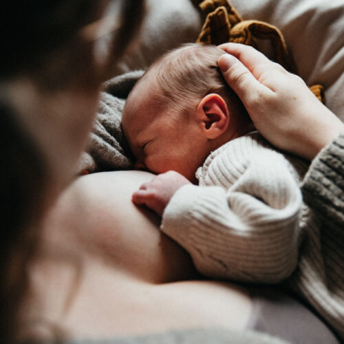 Das Bild zeigt eine Mama beim stillen im Wochenbett wie sie zärtlich den Kopf des Babys streichelt